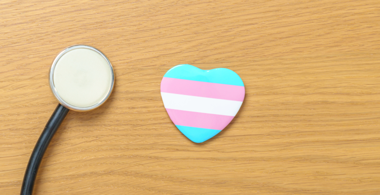 A stethoscope next to a heart with light blue, pink, and white stripes which are the colours of the transgender flag.
