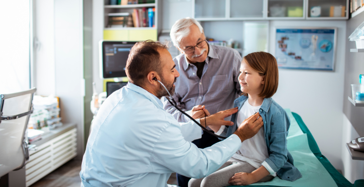 A doctor using a stethoscope to check up on a young patient, who is there with her father.