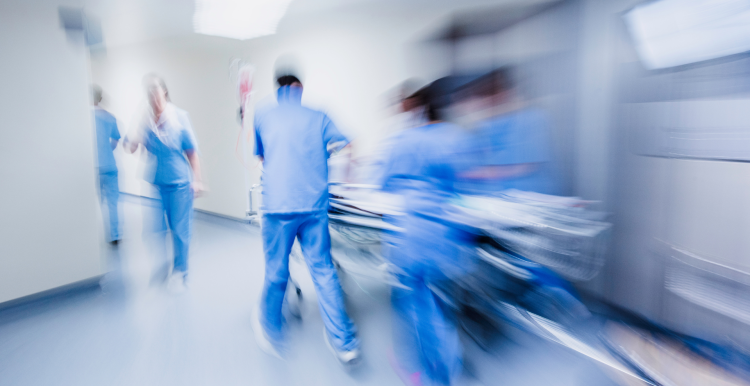 A blurry photo of multiple medical professionals wearing blue scrubs, rushing through a hospital corridor.