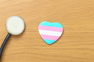 A stethoscope next to a heart with light blue, pink, and white stripes which are the colours of the transgender flag.