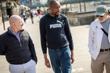 Three men walking together on a pavement.