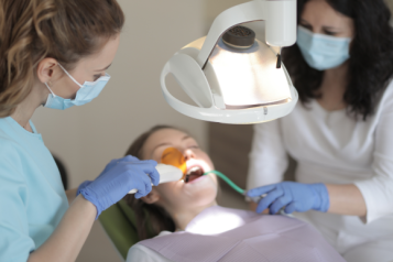 A patient lying on a dentists chair, receiving treatment from two dental professionals.