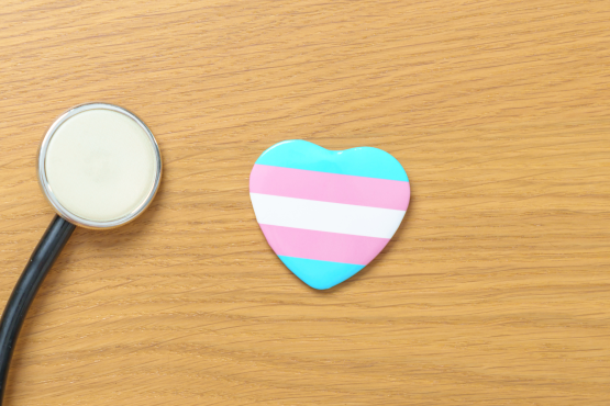 A stethoscope next to a heart with light blue, pink, and white stripes which are the colours of the transgender flag.