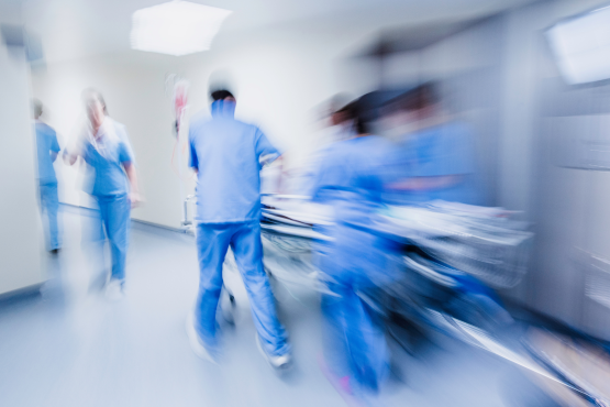 A blurry photo of multiple medical professionals wearing blue scrubs, rushing through a hospital corridor.