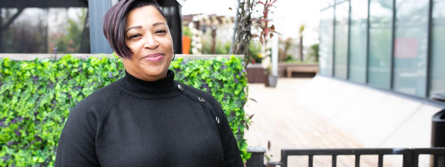 Woman wearing black stood in front of a hedge and building smiling at the camera