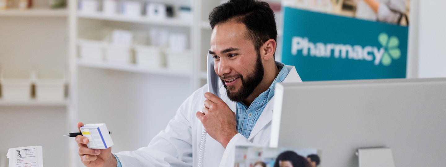 A pharmacist holding a box of medication, on the phone with a customer.