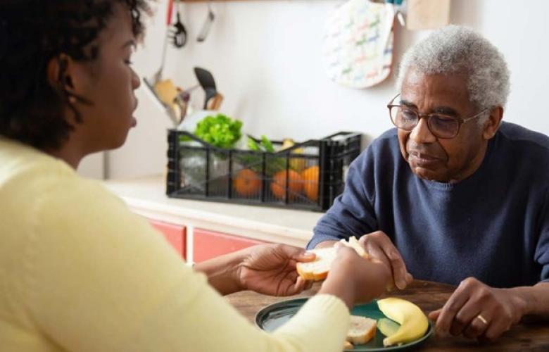 A woman helping an older man eat a meal at a table.