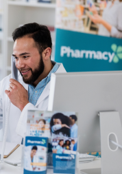 A pharmacist holding a box of medication, on the phone with a customer.